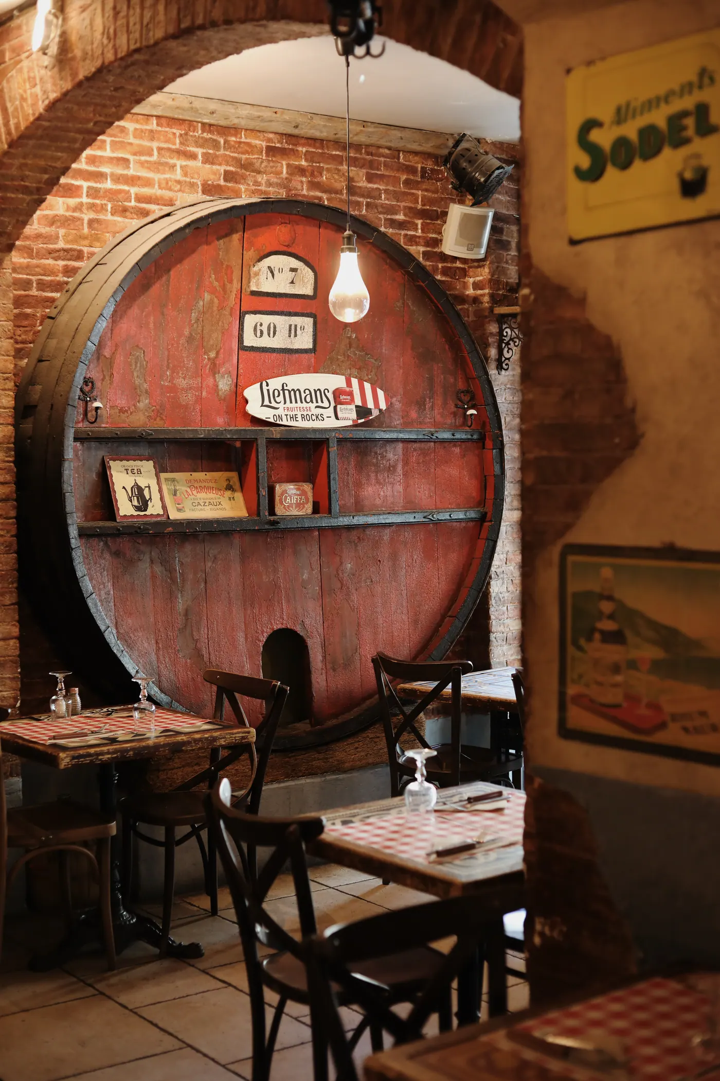 Le foudre en bois rouge de la salle voûtée du Vieux Café, murs de brique et tables à nappes vichy