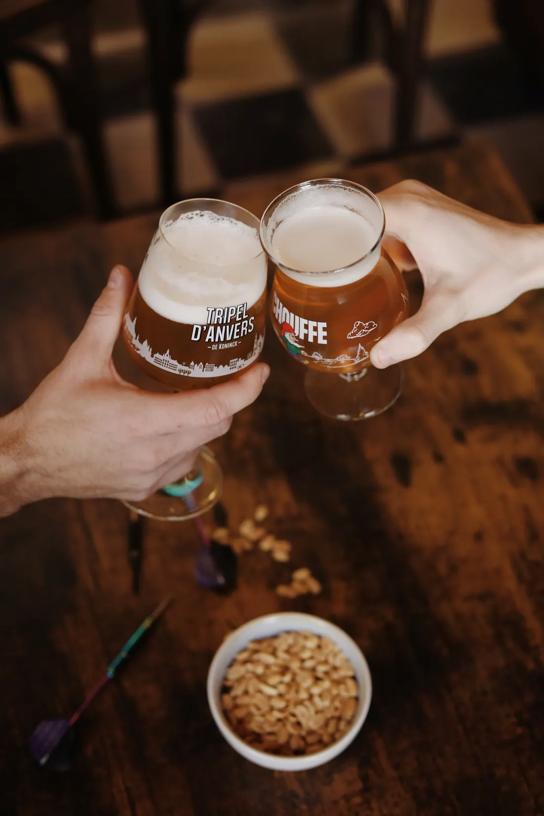 Deux bières belges qui trinquent au-dessus d'une table en bois